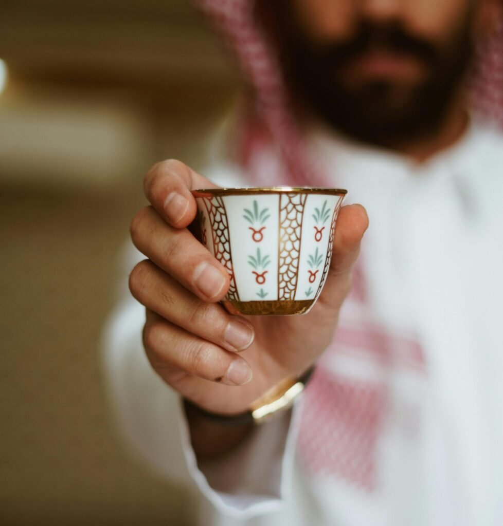 المشهد العام للتواصل المؤسسي في السعودية Close-up of Middle Eastern man in traditional attire offering a decorative cup of coffee.