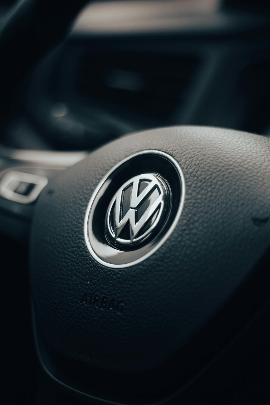 Detail of a Volkswagen steering wheel inside a vehicle's interior. Dark and moody lighting enhances the texture.