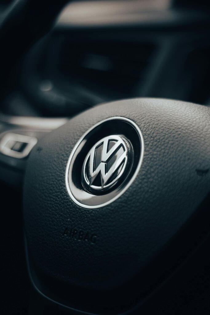 Detail of a Volkswagen steering wheel inside a vehicle's interior. Dark and moody lighting enhances the texture.