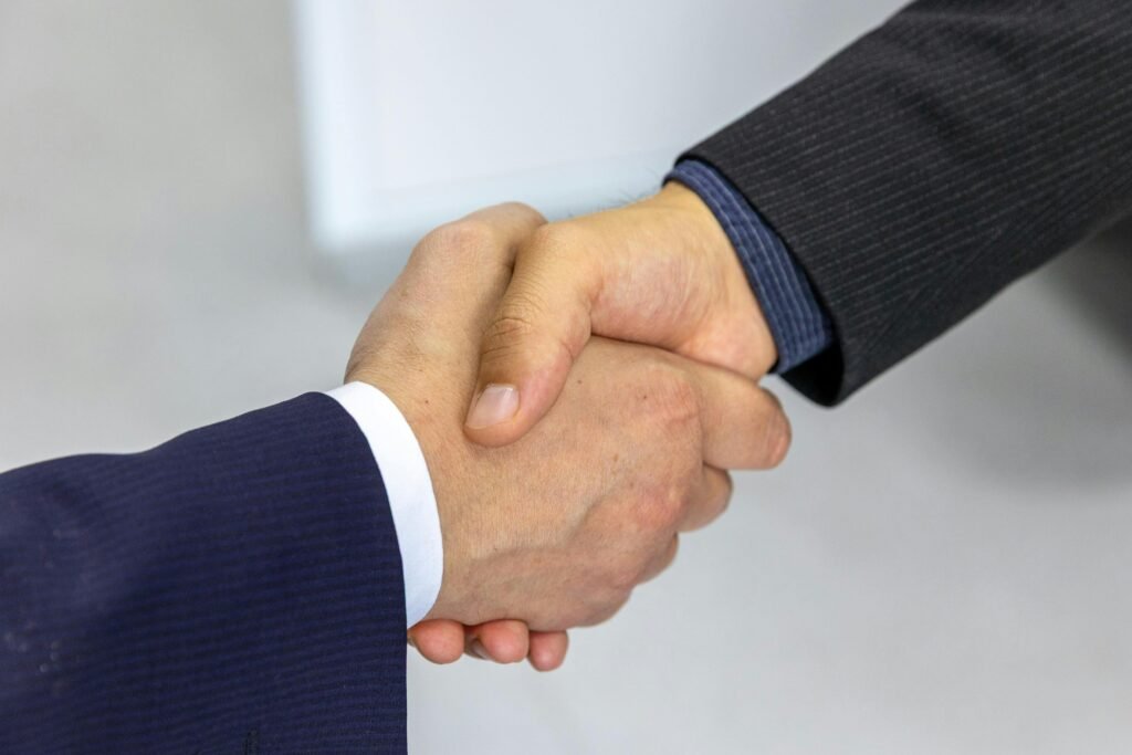 استضافة الاجتماعات باحتراف: قواعد بروتوكولية تصنع الانطباع الأول Close-up of two businessmen shaking hands, symbolizing agreement and partnership.
