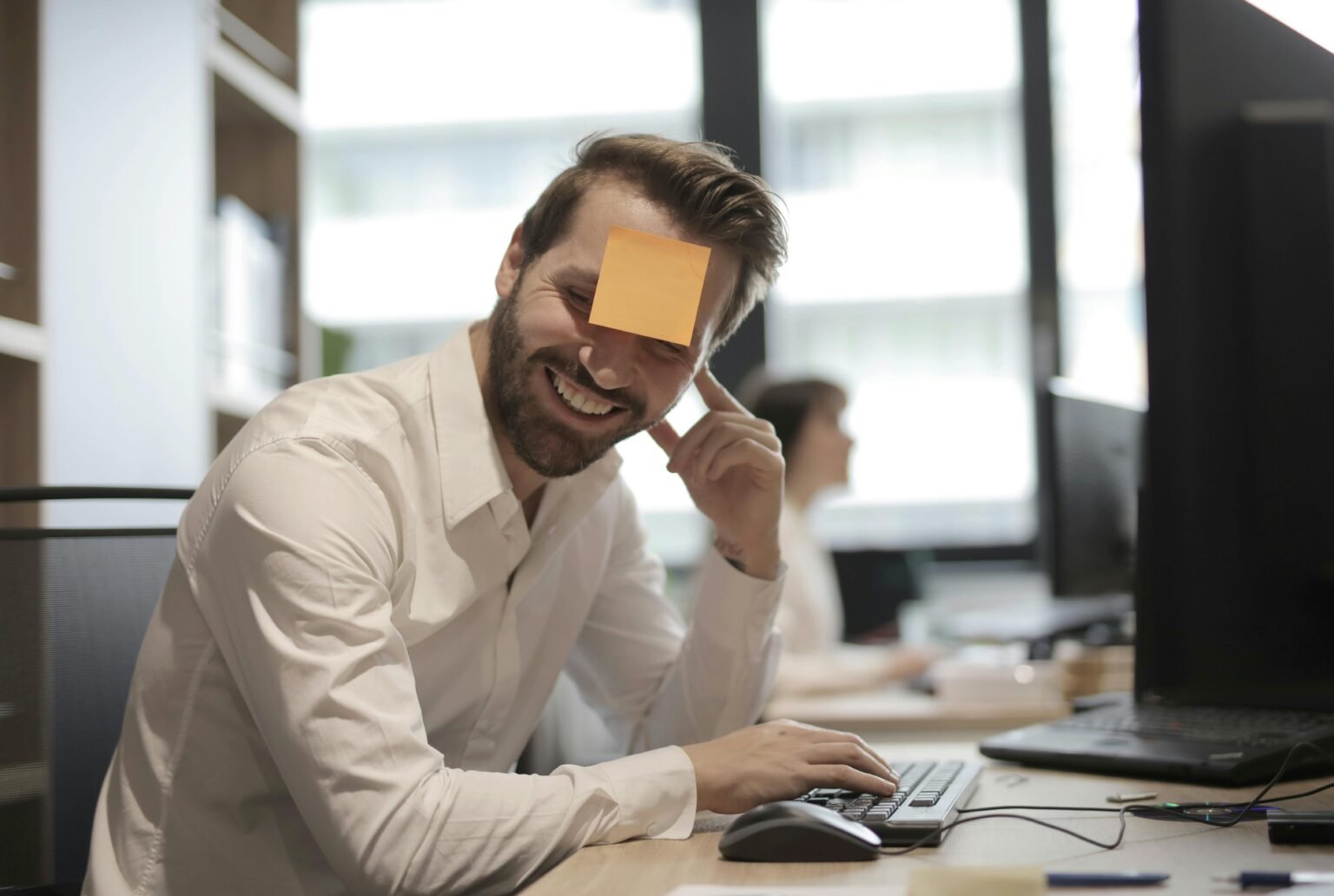 Man having fun with a sticky note on forehead in a modern office setting.