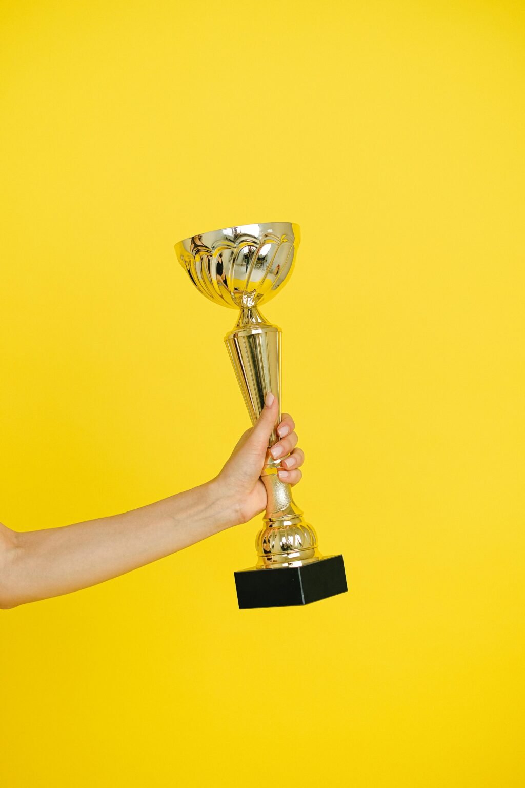 A hand holding a gold trophy against a solid bright yellow background, symbolizing victory.