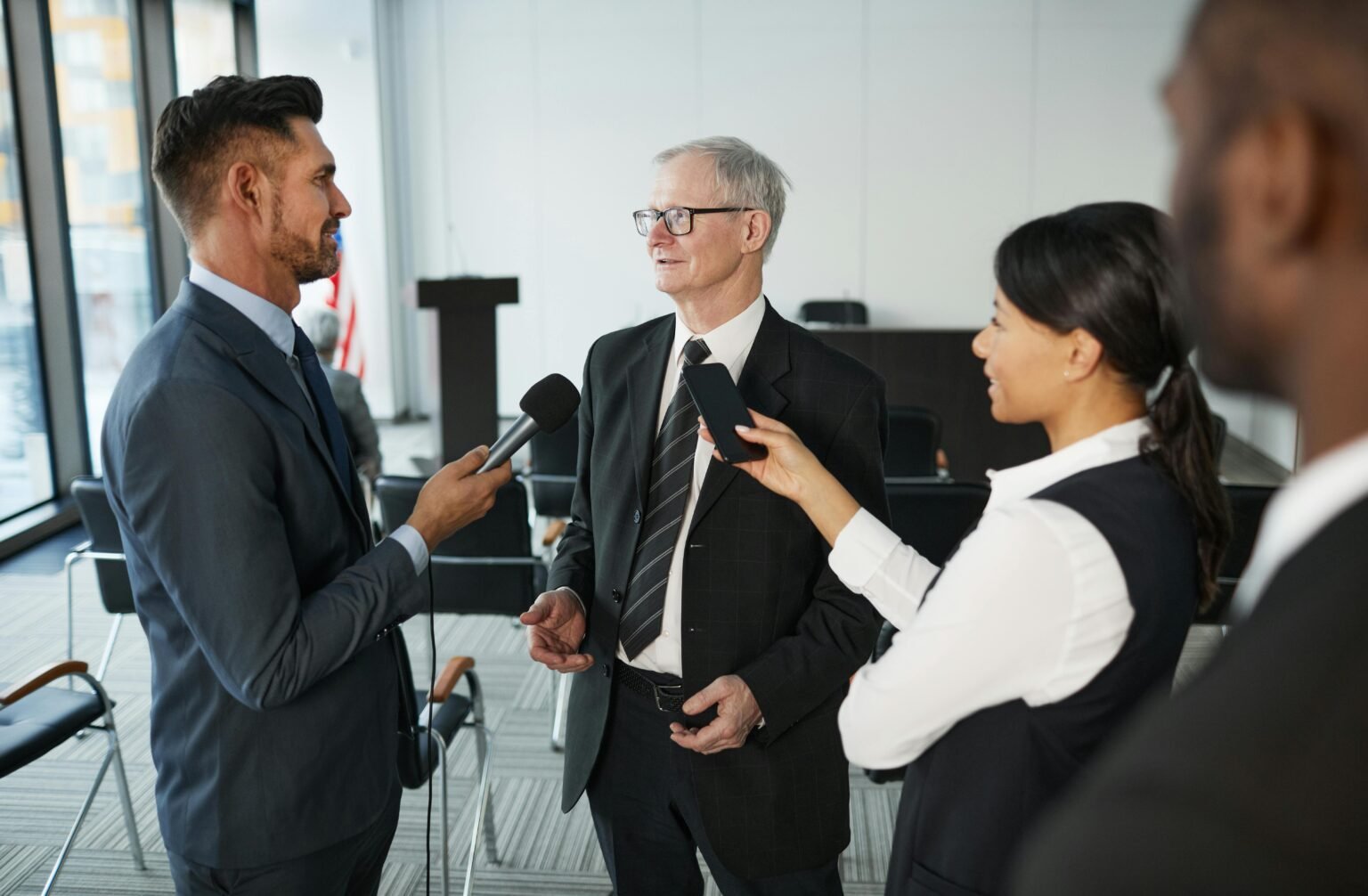 Journalists conduct an interview with a senior executive in a formal office setting.