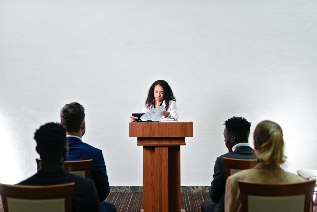 Confident woman delivering a speech to a diverse audience in a conference room.