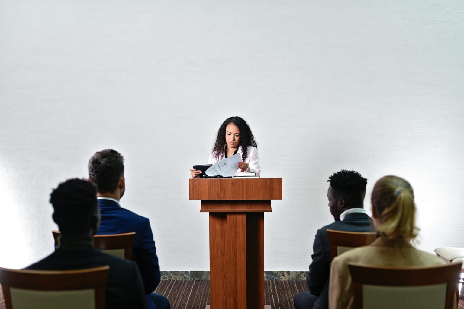 Confident woman delivering a speech to a diverse audience in a conference room.