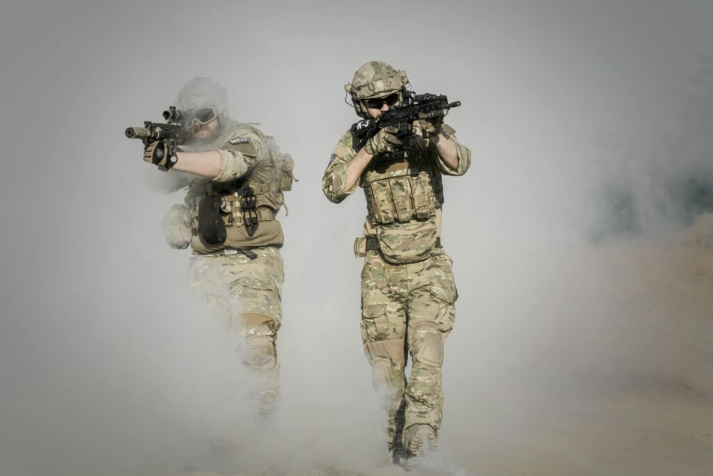 كيف نجح الإعلام الخليجي في إدارة تغطية التصعيد العسكري في المنطقة؟ Two soldiers in camo uniforms with weapons advancing through a smoke-covered field, showcasing military action.
