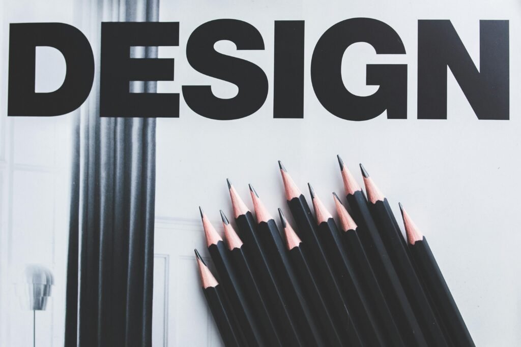 Black pencils arranged creatively next to large typography 'DESIGN'.