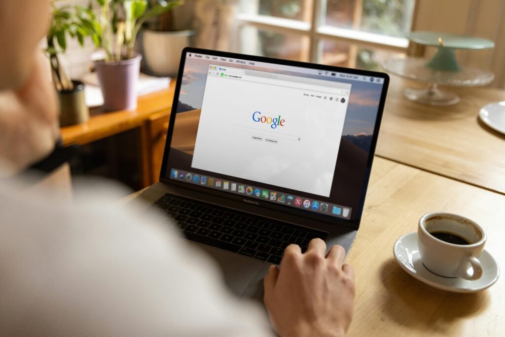 10 مبادرات اتصالية ملهمة تكشف قوة التخطيط الإعلامي المؤسسي An adult using a laptop indoors, browsing Google at a wooden table with coffee.